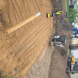 Kop Wiktor Gniado - Żółty rurociąg w wykopie, ubijarka gruntu i mała koparka na placu budowy w słoneczny dzień. Widoczne ślady po przejeździe maszyn.