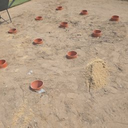 Kop Wiktor Gniado - Przygotowanie terenu pod trawnik: rozmieszczone rury nawadniające na piasku, widoczna taczka i fragment trawnika w tle. Etap prac ziemnych.