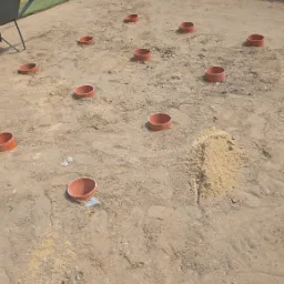 Przygotowanie terenu pod trawnik: rozmieszczone rury nawadniające na piasku, widoczna taczka i fragment trawnika w tle. Etap prac ziemnych.