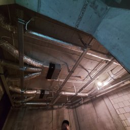 Kop Wiktor Gniado - Widok instalacji wentylacyjnej z rurami spiro i centralą wentylacyjną pod betonowym stropem, z widocznymi elementami montażowymi i oświetleniem roboczym.