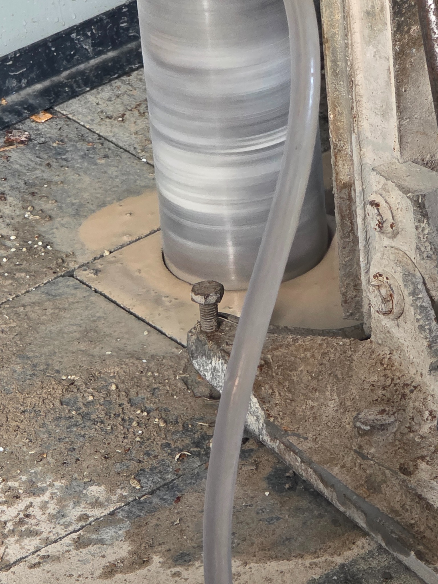 Wiertnica rdzeniowa w trakcie pracy, wiercenie w płytach chodnikowych, widoczny osprzęt i woda chłodząca. Detal ujęcia z bliska, szare barwy.