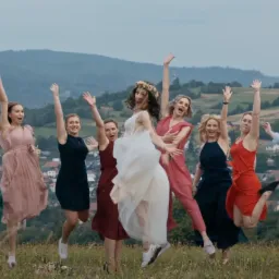 Panna młoda z druhnami skaczą radośnie na tle g&oacute;rskiego krajobrazu, uchwycone z niskiej perspektywy.