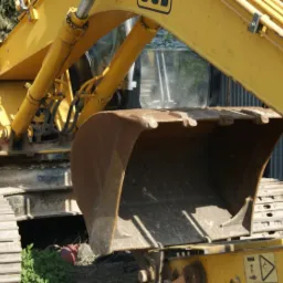 Żółta koparka JCB z widocznym łyżką i gąsienicami, zaparkowana na zewnątrz, z bliska.