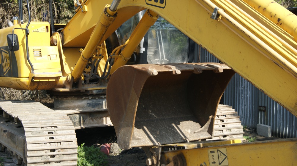 Żółta koparka JCB z widocznym łyżką i gąsienicami, zaparkowana na zewnątrz, z bliska.