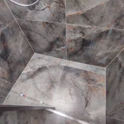 Szare płytki imitujące marmur w kabinie prysznicowej z odpływem liniowym i widoczną słuchawką prysznicową