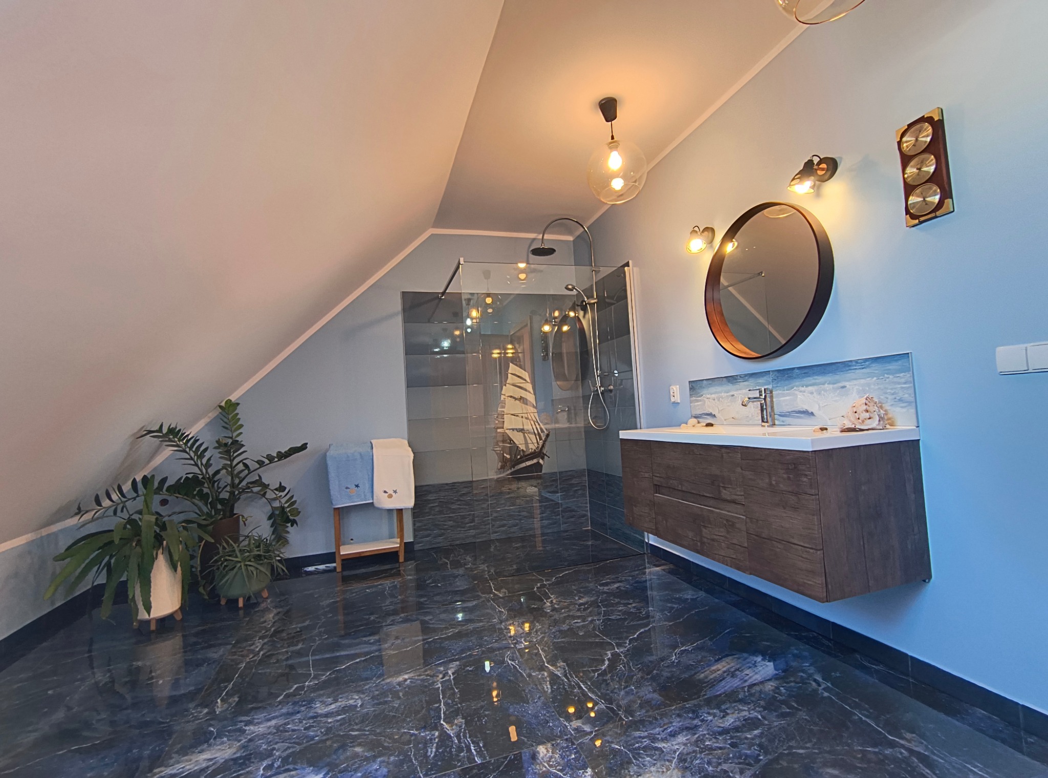 Nowoczesna łazienka na poddaszu z kabiną prysznicową typu walk-in, umywalką z szafką w kolorze ciemnego drewna, lustrem w okrągłej ramie i dekoracjami w stylu marynistycznym.