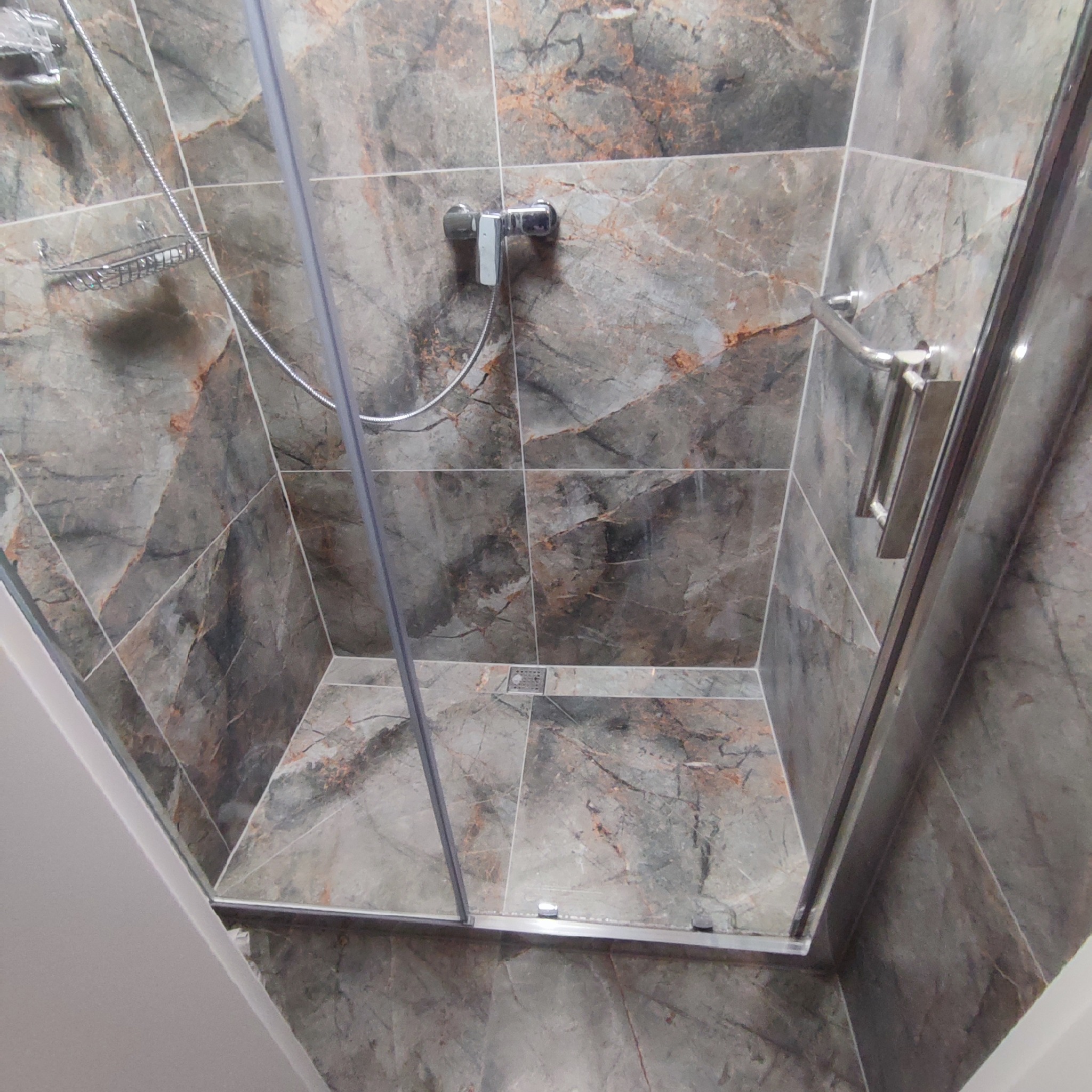 Kabina prysznicowa z szarymi płytkami imitującymi marmur, chromowana armatura i półka na kosmetyki, widok z góry.