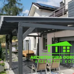 Ciemnoszara pergola z przezroczystym zadaszeniem przylegająca do domu, widoczne krzesła ogrodowe i elementy zieleni.