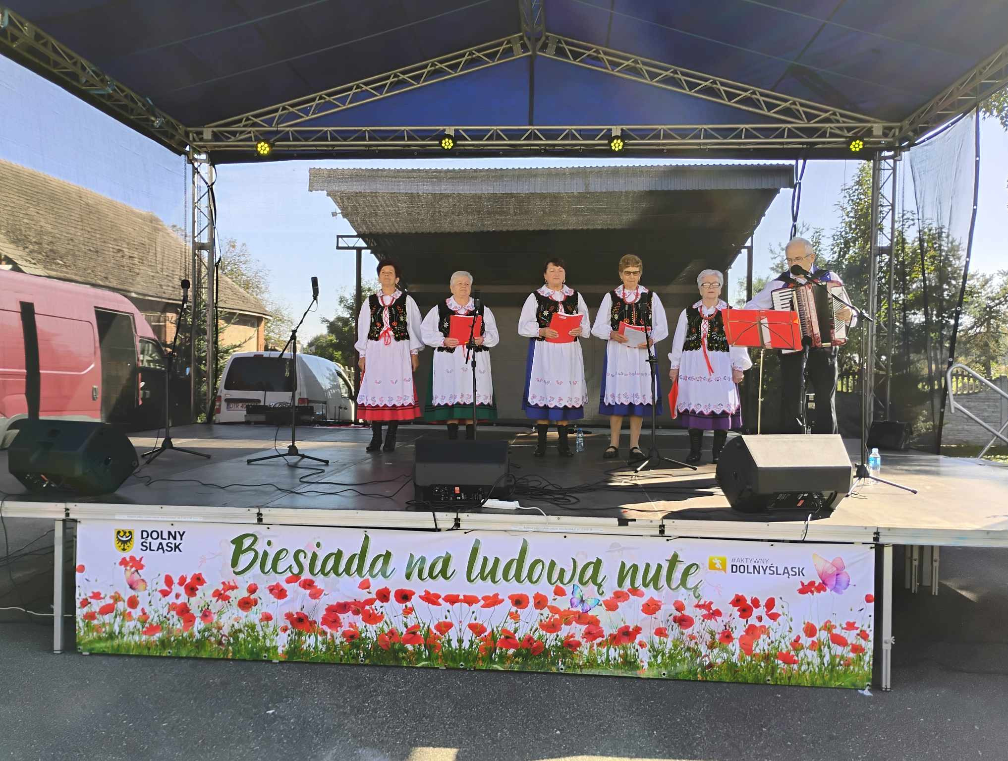Zespół ludowy w tradycyjnych strojach występuje na scenie podczas plenerowej imprezy 'Biesiada na ludową nutę', akordeonista po prawej stronie.
