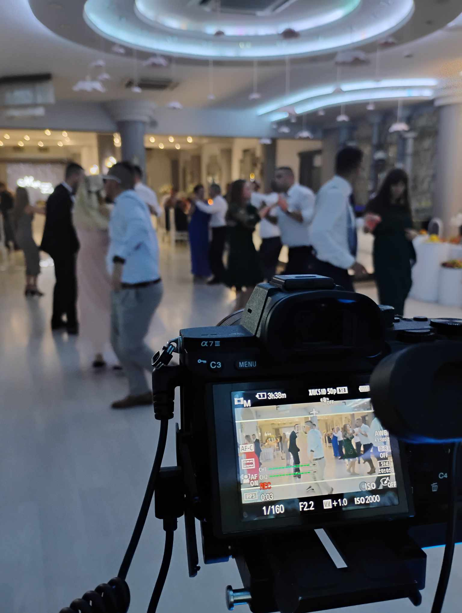 Ekran aparatu Sony Alpha 7 III rejestrujący taniec weselny w sali balowej z dekoracyjnym oświetleniem sufitowym. Parametry ekspozycji: 1/160 s, f/2.2, ISO 2000.