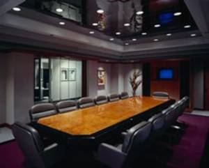 Sala konferencyjna z długim stołem z polerowanego drewna, otoczonym przez krzesła z szarej skóry. Na ścianach obrazy i dekoracyjny element przypominający gałęzie. Sufit z ciemnego, błyszczącego...