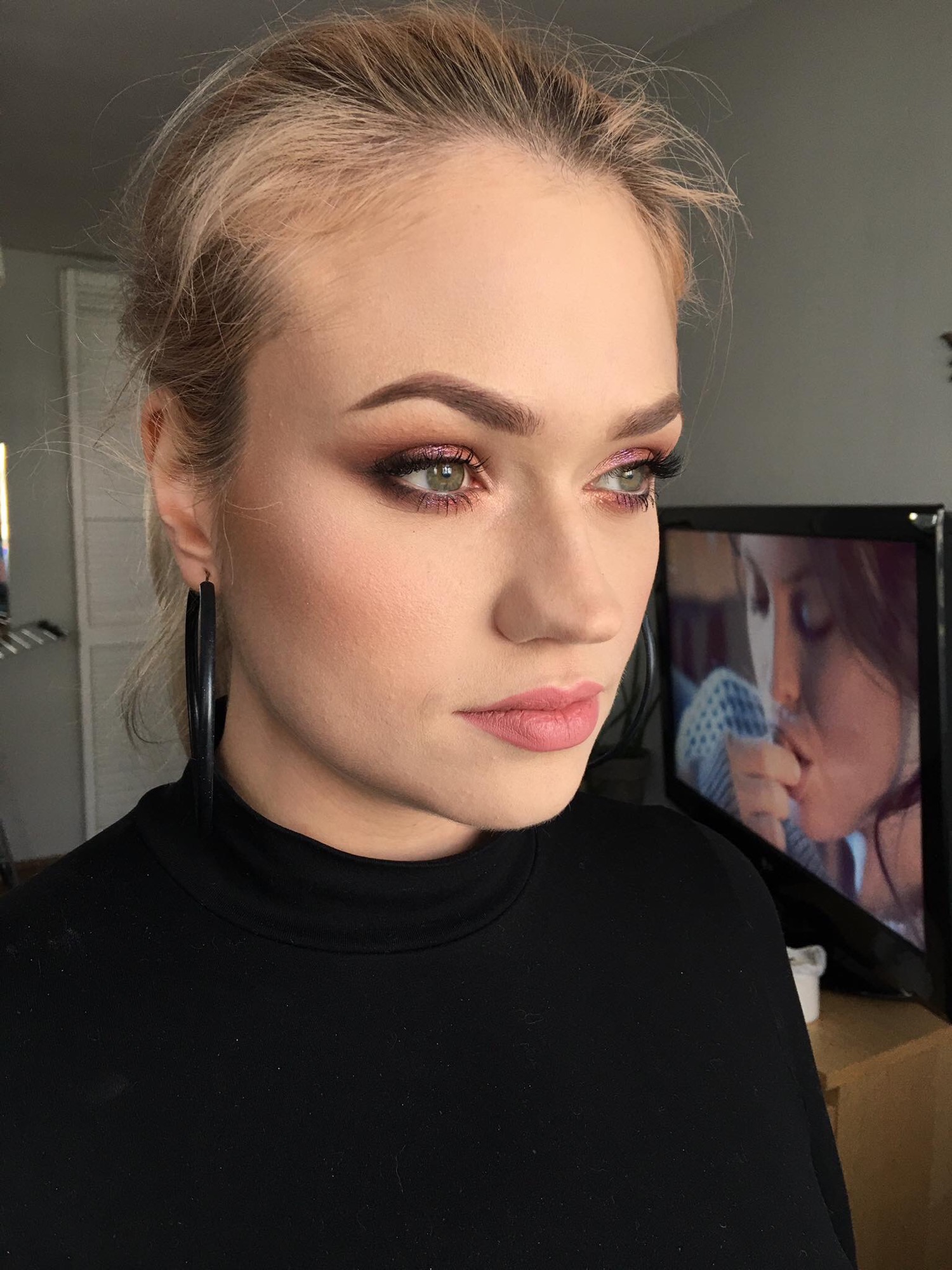 Portret kobiety z profesjonalnie wykonanym, subtelnym makijażem oczu w odcieniach różu i brązu, z widocznymi długimi rzęsami i delikatnym różem na policzkach, patrzącej w bok, z dużymi czarnymi...