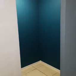 Narożnik pomalowany na intensywny, ciemny odcień niebieskiego w mieszkaniu w Świerznie, widoczne jasne płytki podłogowe i biała listwa przypodłogowa, kontrastujące z szarymi elementami...