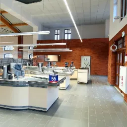 Nowoczesne wnętrze sklepu z kasami samoobsługowymi, ceglaną ścianą i drewnianą konstrukcją dachu w stylu industrialnym.