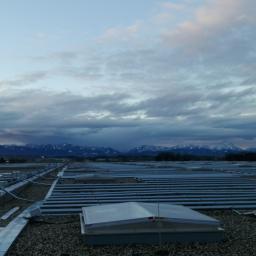Mako Maciej Marcinów - Rozległa instalacja fotowoltaiczna na dachu pokrytym żwirem, w tle widoczne pasmo górskie pod pochmurnym niebem.
