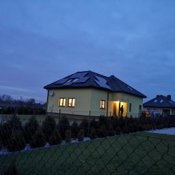 Mako Maciej Marcinów - Dom jednorodzinny z panelami słonecznymi na dachu, widoczny zza ogrodzenia w Brzesku, oświetlony wieczorną porą.