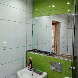 Bos-Bud - Łazienka w trakcie remontu: białe i zielone płytki, niedokończona zabudowa lustra, umywalka z płynem do czyszczenia, widoczne elementy instalacji.