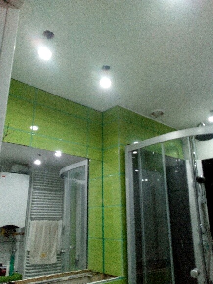 Łazienka w trakcie remontu: zielone płytki ułożone na ścianach, widoczne linie wyznaczające fugi, zamontowana kabina prysznicowa z przezroczystego szkła, grzejnik drabinkowy i biały bojler na ścianie.