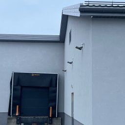 Chrzan-Dach - Zewnętrzny widok budynku z szarą elewacją, widoczne obróbki blacharskie dachu i trzy czarne kamery na ścianie