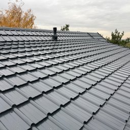 Chrzan-Dach - Nowoczesny, grafitowy dach z dachówki modułowej, z kominkiem wentylacyjnym i oknem dachowym, na tle jesiennego krajobrazu i pochmurnego nieba.