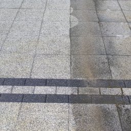 ZACZYSZCZONE PIOTR STĘPNIAK - Granitowa kostka brukowa częściowo umyta, widoczna różnica w kolorze i czystości między umytą a nieumytą powierzchnią, z ciemniejszym pasem kostki oddzielającym obszary.