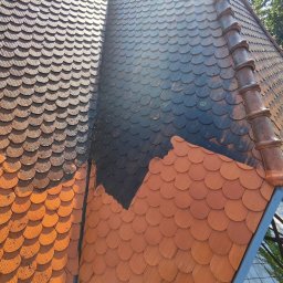 ZACZYSZCZONE PIOTR STĘPNIAK - Częściowo wyczyszczony dach z łuski ceramicznej, ukazujący różnicę w kolorze i czystości. Widoczne zabrudzenia i odświeżona powierzchnia.