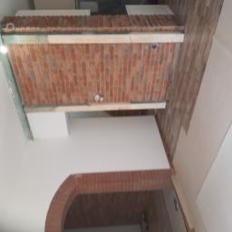 Mawix Sp z.o.o - Wnętrze w trakcie prac wykończeniowych: fragment ściany z cegły klinkierowej, drewniane elementy konstrukcyjne, fragment łuku z cegły, panele podłogowe i białe ściany.