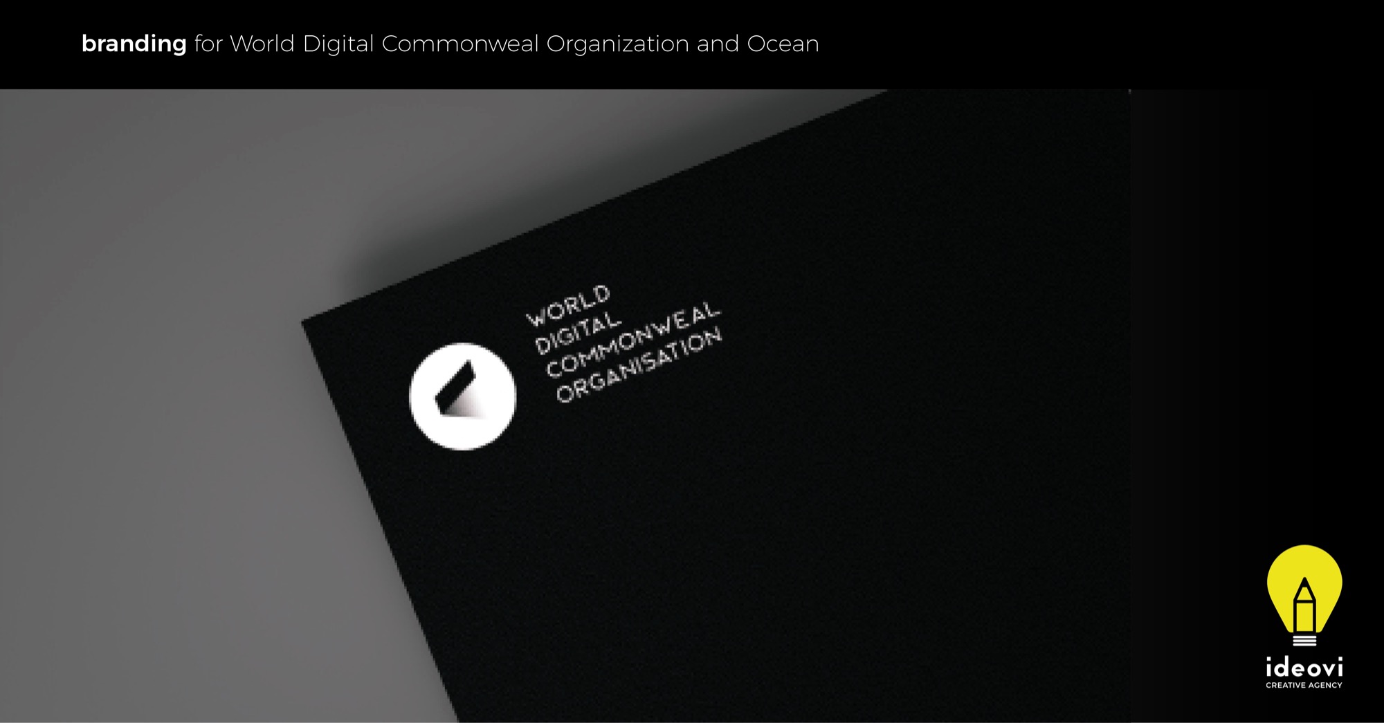 Czarny kartonik z logo i nazwą 'World Digital Commonweal Organisation' w kolorze białym, leżący na szarym tle, w prawym dolnym rogu logo agencji 'Ideovi'.