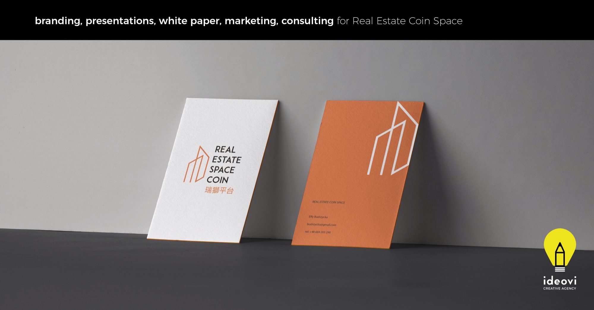 Dwie wizytówki firmy Real Estate Coin Space, jedna biała z logo i nazwą w kolorze miedzianym, druga miedziana z białym logo, ustawione pod kątem na szarym tle, w prawym dolnym rogu logo agencji...