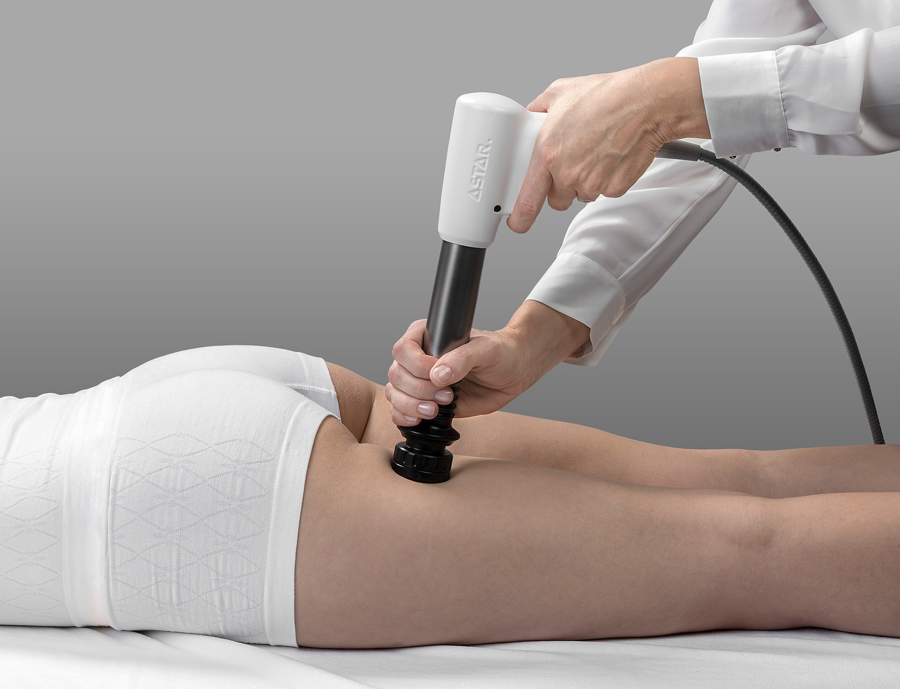 Osoba poddawana zabiegowi z użyciem urządzenia Astar na tylnej części uda, w gabinecie z szarym tłem.