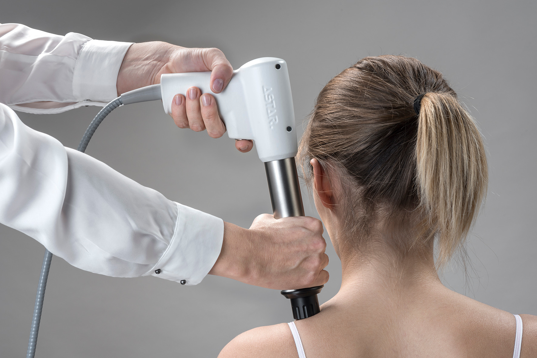 Fizjoterapeuta wykonuje zabieg na szyi pacjentki za pomocą urządzenia do fizykoterapii marki ASTAR.