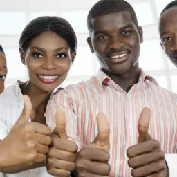 Cztery uśmiechnięte osoby z podniesionymi kciukami, symbolizujące sukces i zadowolenie, w tle jasne biuro.