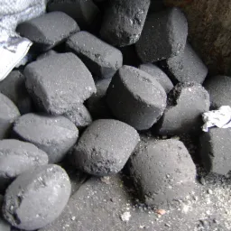 Ciemnoszare, cylindryczne bryły paliwa w worku jutowym, widoczne drobne pęknięcia i nierówności na powierzchni, biały fragment materiału między bryłami.