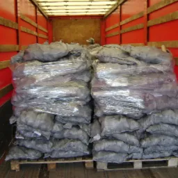 Wnętrze czerwonej ciężarówki wyładowane workami ekogroszku na palecie, zabezpieczonymi folią stretch.