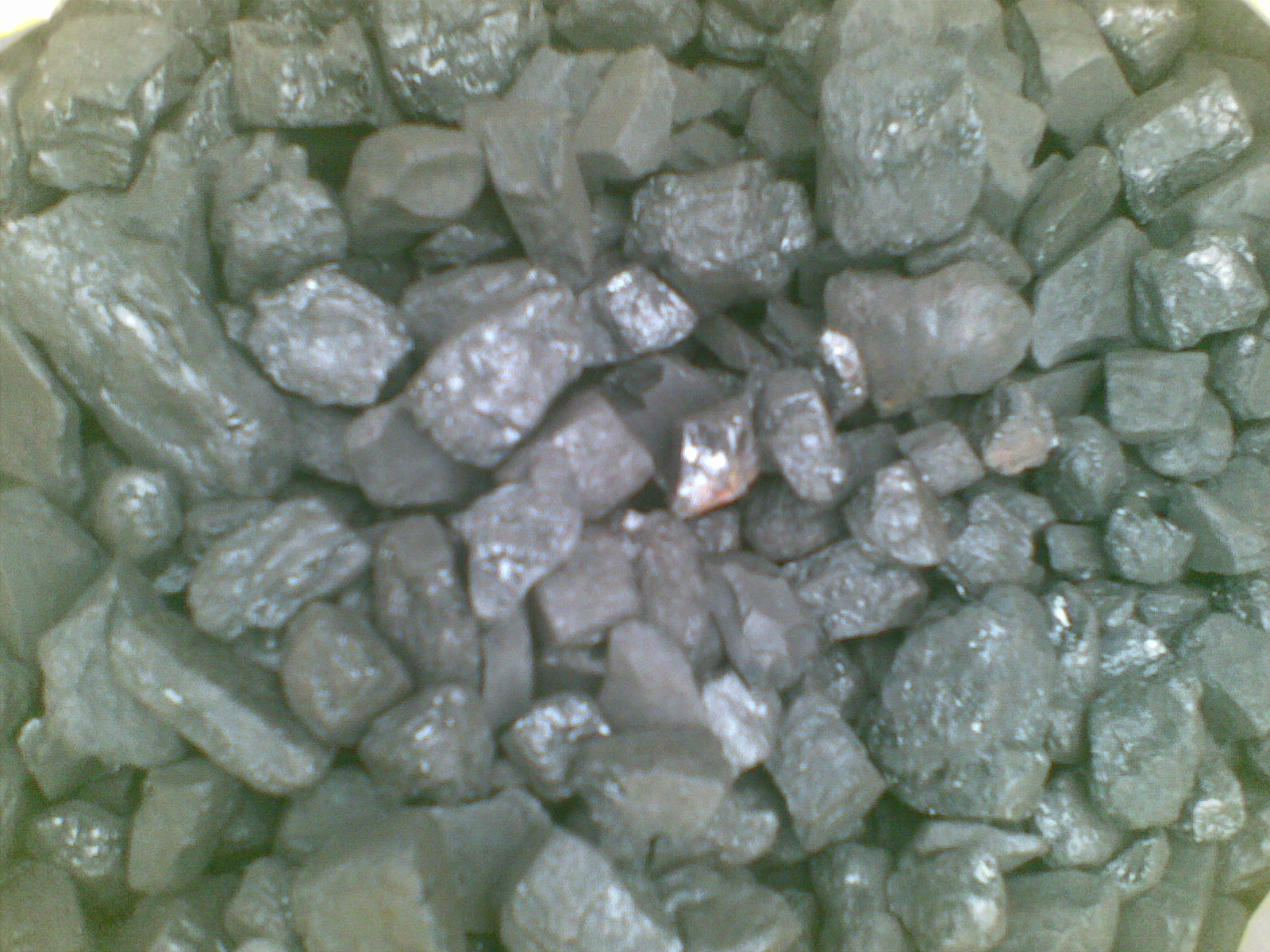 Kupa antracytu o nieregularnych kształtach i matowej powierzchni, oświetlona z góry, ukazująca różnorodność odcieni szarości i czerni.