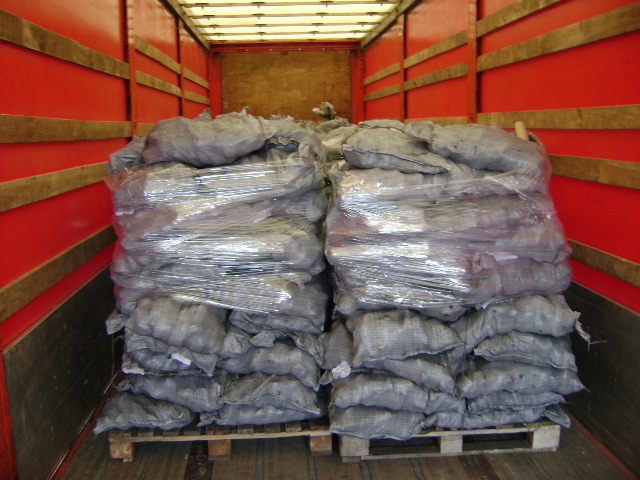 Wnętrze czerwonej ciężarówki wyładowane workami ekogroszku na palecie, zabezpieczonymi folią stretch.