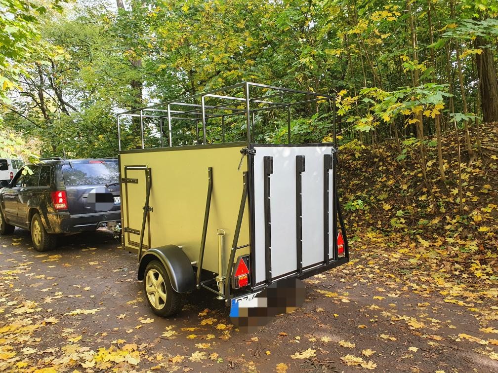 Przyczepa ślusarska z metalową konstrukcją, podłączona do samochodu na leśnej drodze pokrytej liśćmi.