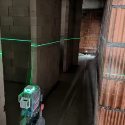 Laser krzyżowy Bosch generuje zielone linie na surowych ścianach z betonu komórkowego i cegły ceramicznej podczas prac pomiarowych wewnątrz budynku w stanie deweloperskim.