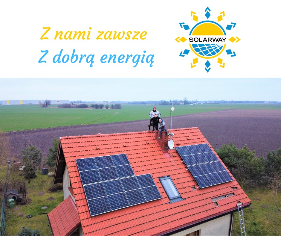 Instalacja fotowoltaiczna na dachu domu z czerwoną dachówką, trzech monterów siedzi na kominie, w tle zielone pola i logo Solarway