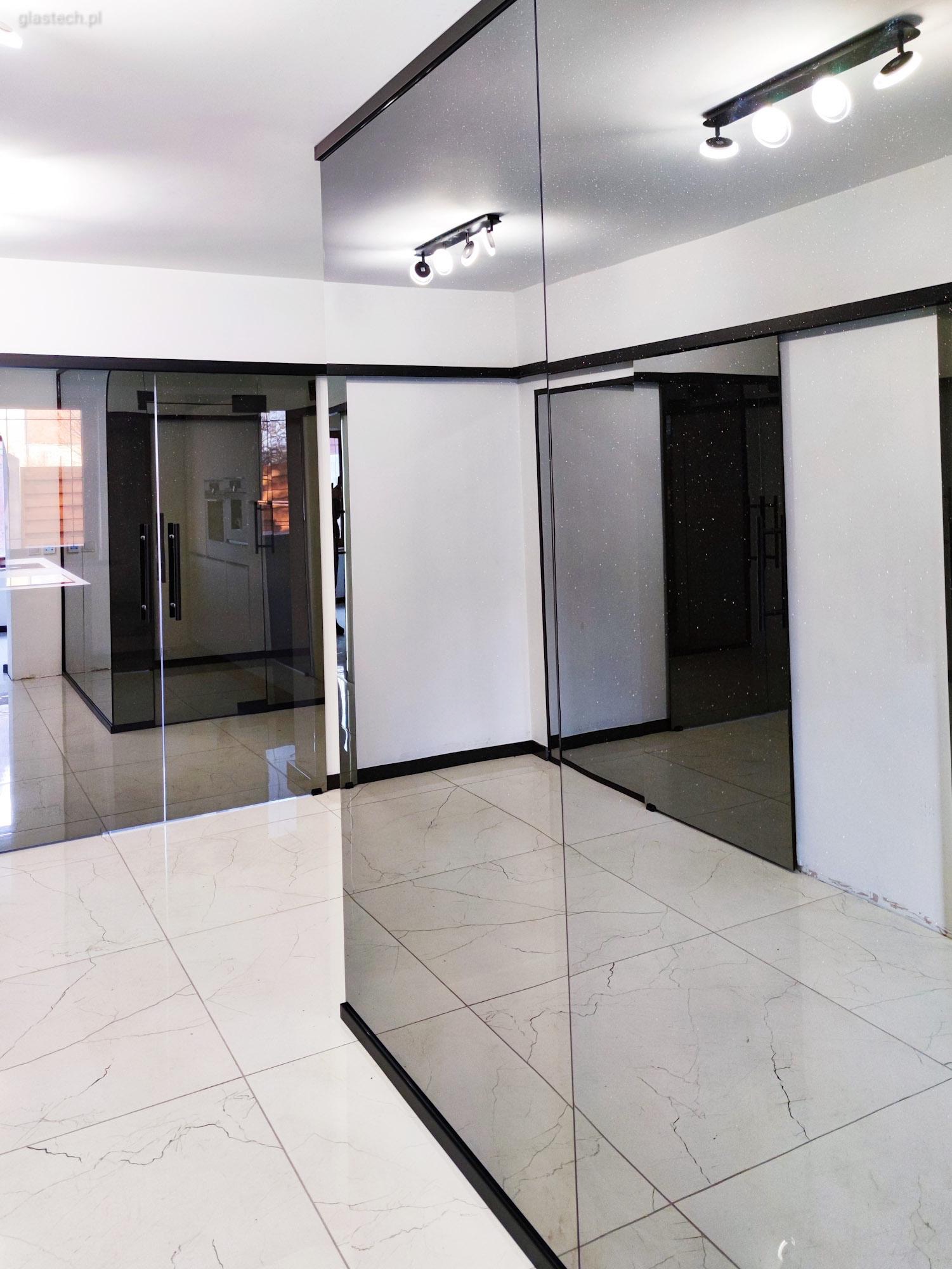 Szklane ściany działowe z czarnymi ramami w biurze w Wałbrzychu, odbijające światło lamp sufitowych i wzór marmurowej podłogi.