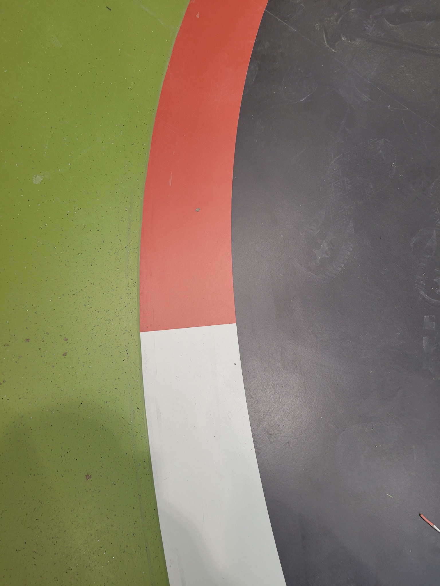 Fragment podłogi z zieloną, szarą i czerwoną wykładziną tworzącą zakrzywiony wzór.