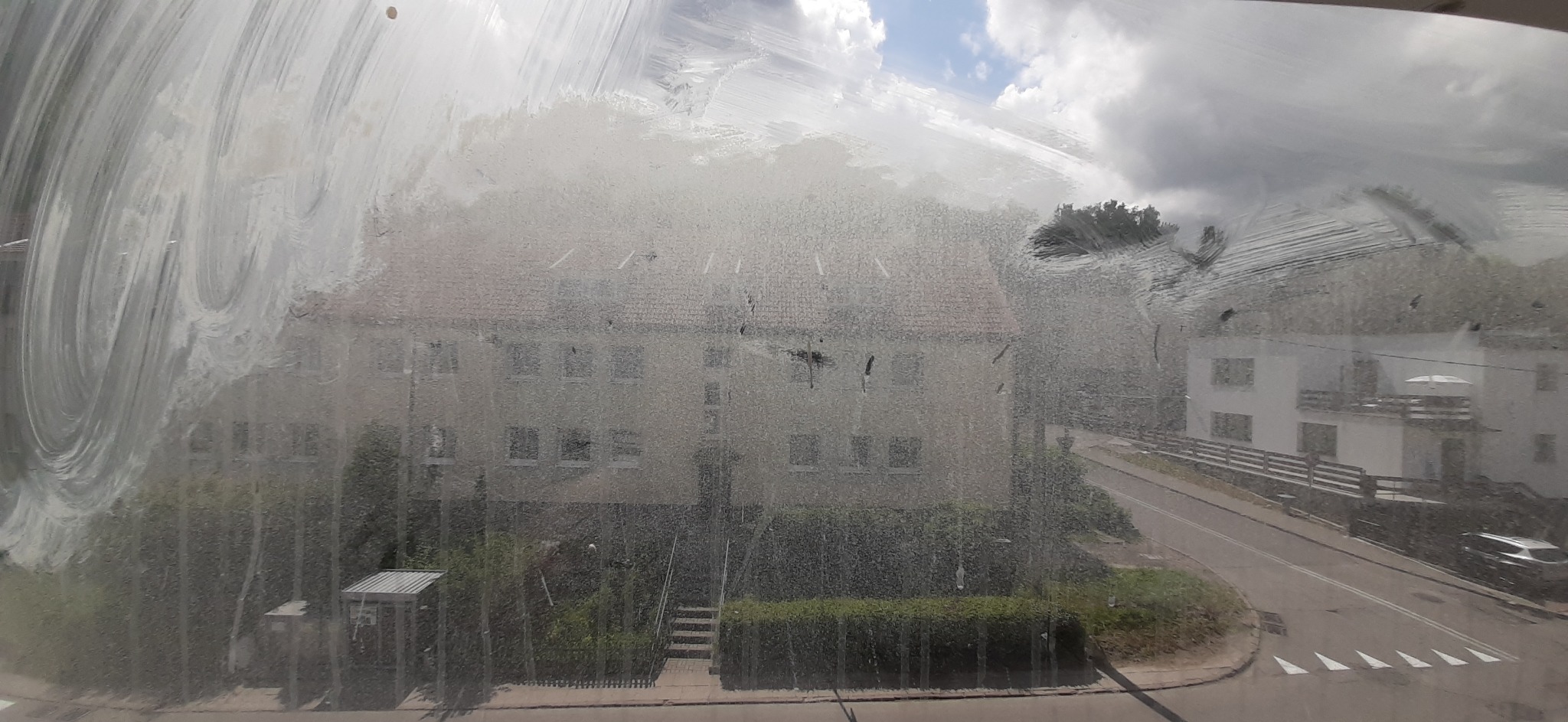 Silnie zabrudzone okno z widokiem na budynek mieszkalny i ulicę. Na szybie widoczne smugi i zacieki po nieudanym myciu.