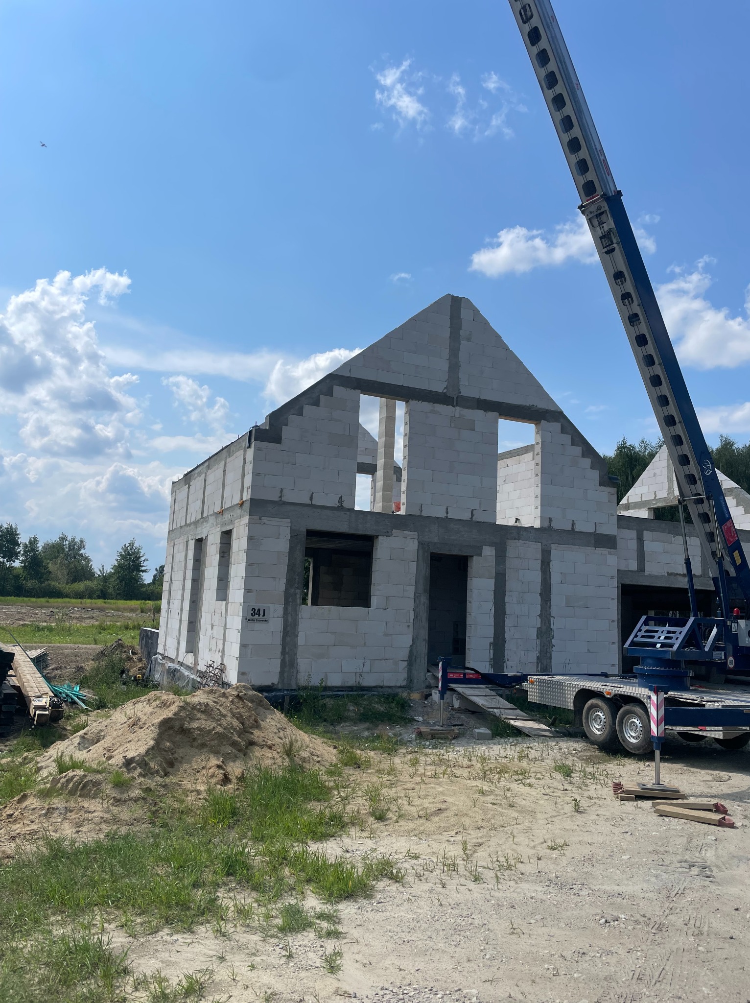 Budowa domu z betonu komórkowego w słoneczny dzień. Widoczny dźwig i elementy konstrukcyjne. Stan surowy otwarty, zarys dachu.