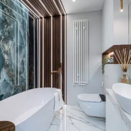 Luksusowa łazienka z wolnostojącą wanną, marmurową podłogą i ścianą z onyksu podświetloną ledami. Nowoczesny design z elementami drewna i armaturą w kolorze różowego złota.