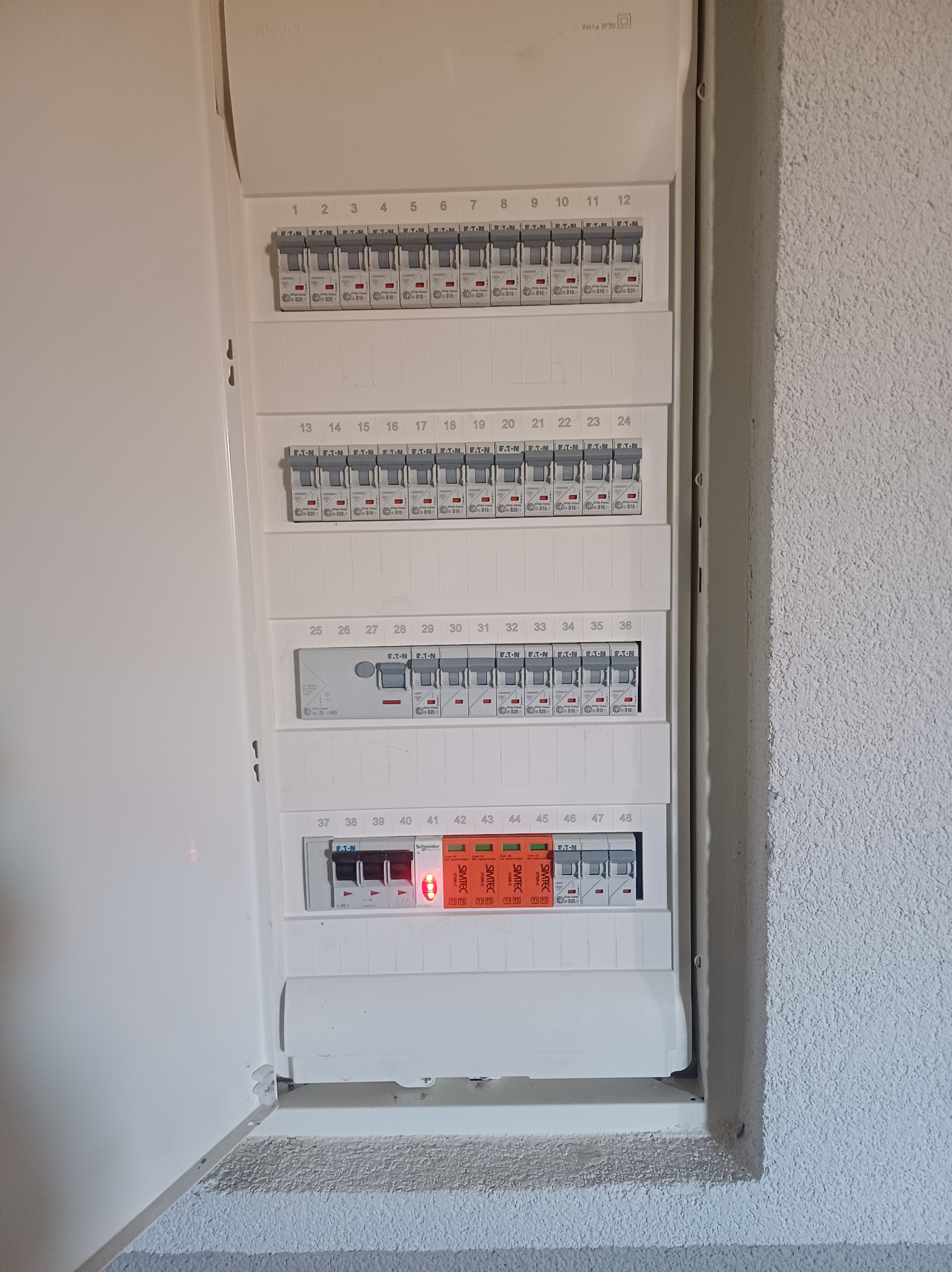 Otwarta skrzynka bezpiecznikowa z widocznymi bezpiecznikami różnych typów i marek, w tym Eaton i Schneider, z niektórymi włączonymi i jednym z czerwonym wskaźnikiem zadziałania, zamontowana...