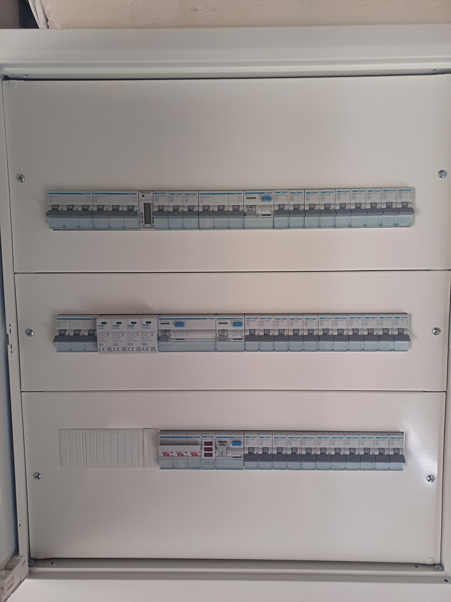 Rozdzielnica elektryczna z trzema rzędami zabezpieczeń Hager, widoczne bezpieczniki różnicowoprądowe i nadprądowe, zainstalowana w obudowie natynkowej.