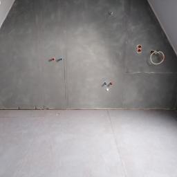 Marcin Palarski FHU - Pokój na poddaszu w trakcie przygotowania do prac wykończeniowych: szare ściany z wyprowadzonymi instalacjami wodno-kanalizacyjnymi i elektrycznymi, szara podłoga, widoczne łączenia płyt...