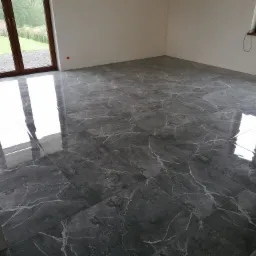 Ułożona, błyszcząca, ciemnoszara glazura imitująca marmur z białymi żyłkami, widoczna w nowym pokoju w Mucharzu, z dużym oknem balkonowym i widokiem na zieleń.