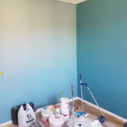 Pokój po malowaniu ścian na dwa odcienie błękitu, widoczne narzędzia malarskie i puszki z farbą.