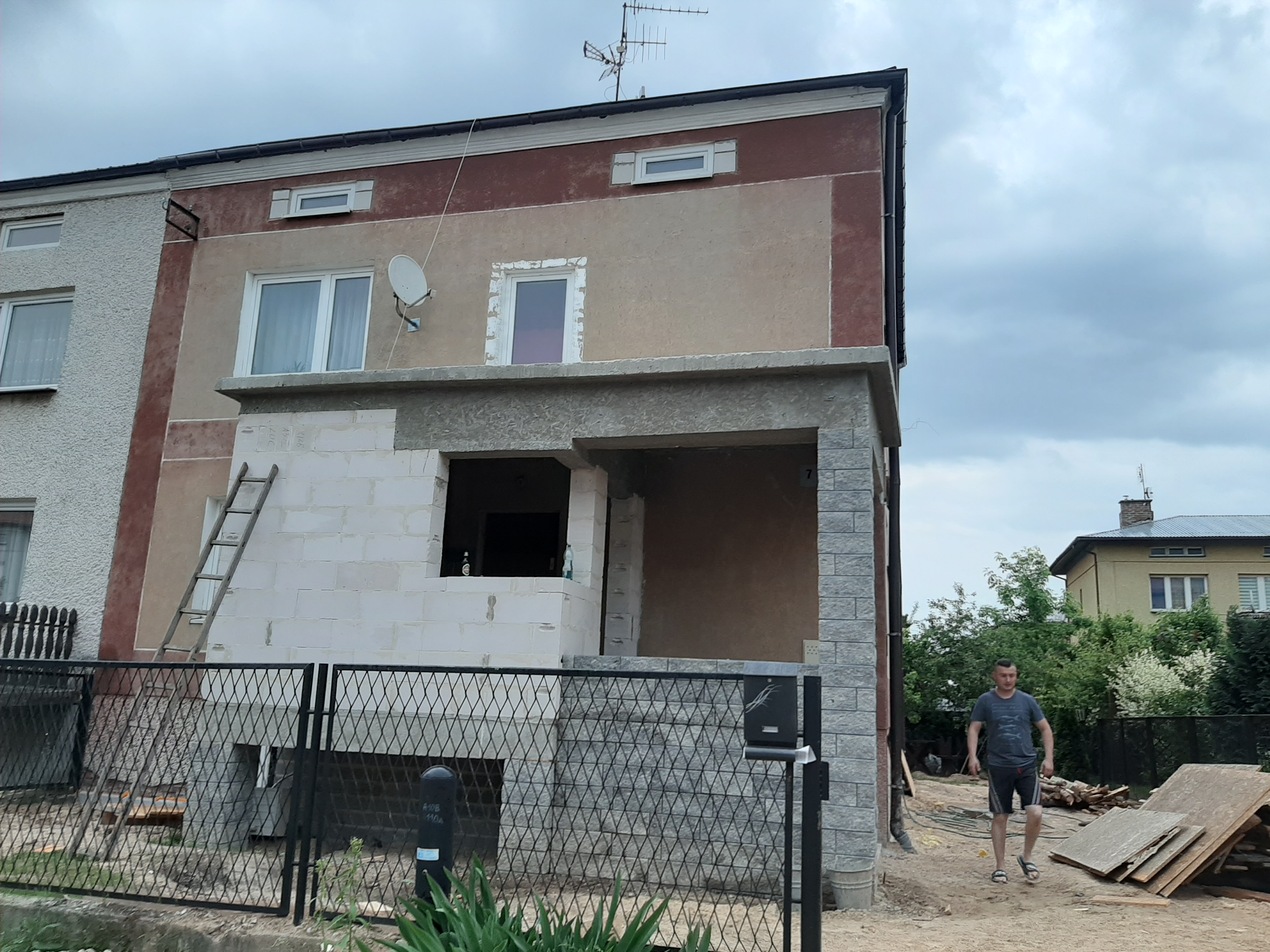 Budynek w Zamościu w trakcie remontu elewacji z widocznymi blokami betonowymi, rusztowaniem i elementami dekoracyjnymi z szarej cegły na werandzie.